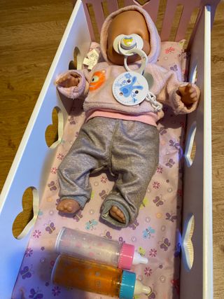 Cuna de juguete con muñeca y acesorios.