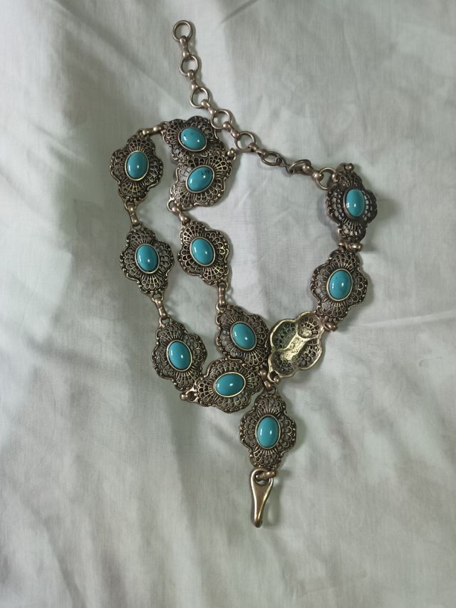 Cinturón metálico con adornos azules.