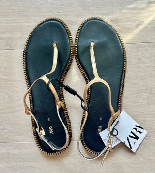 Sandalias doradas planas con la etiqueta.