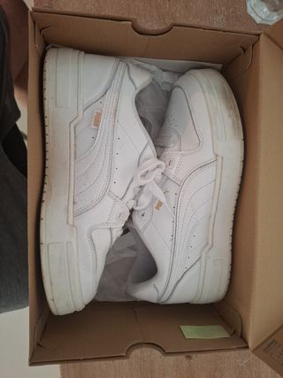 Zapatillas Puma blancas con detalles dorados.