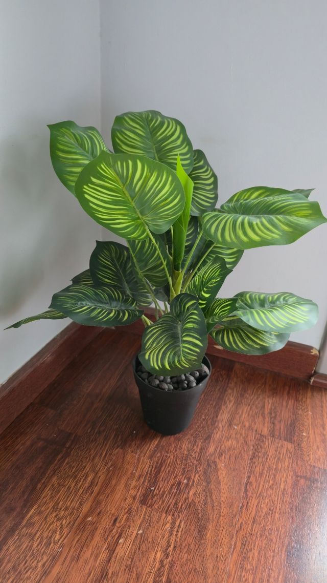 Macetero blanco de mimbre y planta artificial.