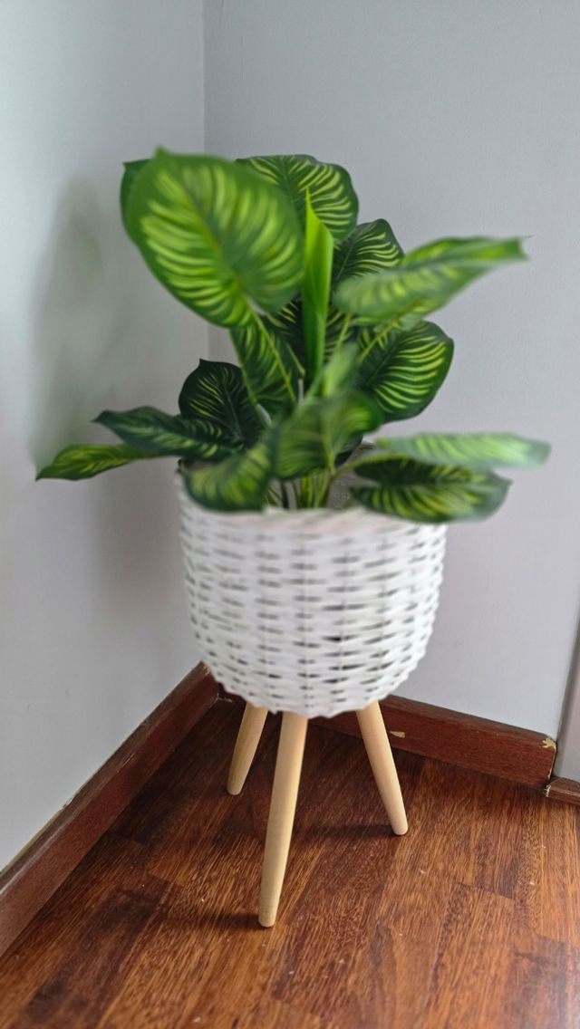 Macetero blanco de mimbre y planta artificial.