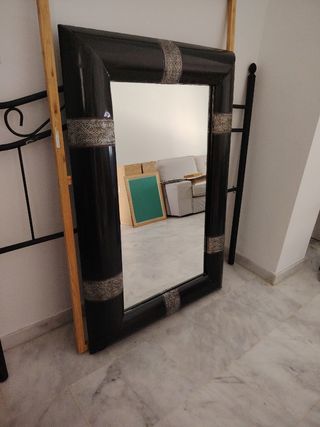 Espejo con marco negro y filigrana plateada. 