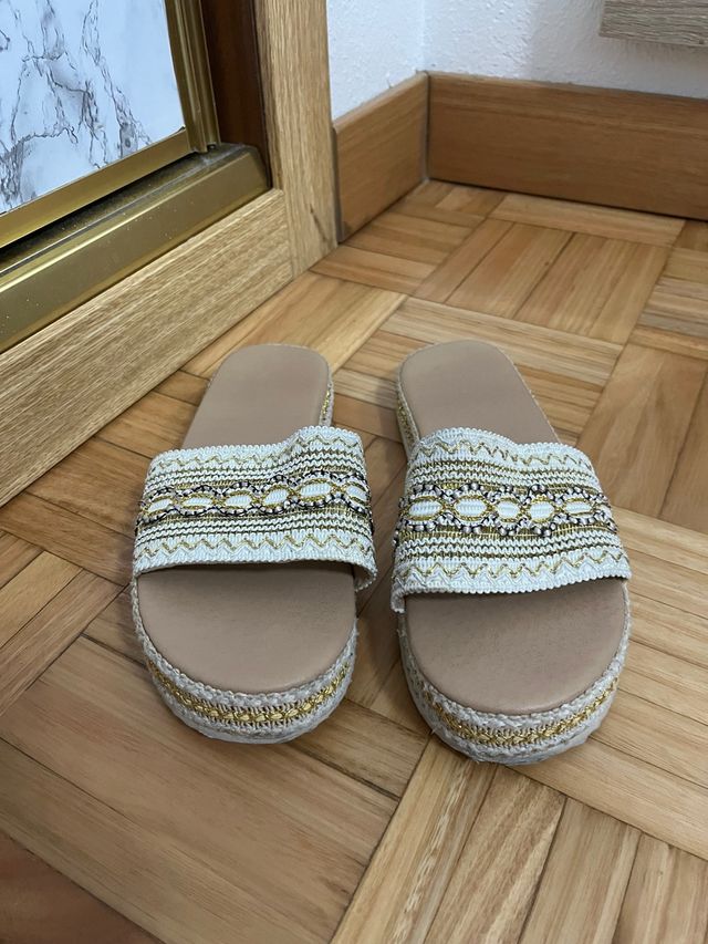 Sandalias planas beige y doradas.