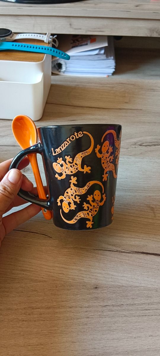 Taza negra con lagartos naranjas y cucharilla