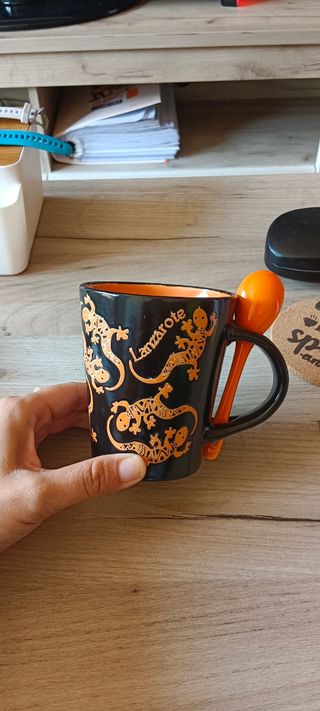 Taza negra con lagartos naranjas y cucharilla