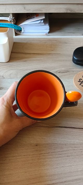 Taza negra con lagartos naranjas y cucharilla