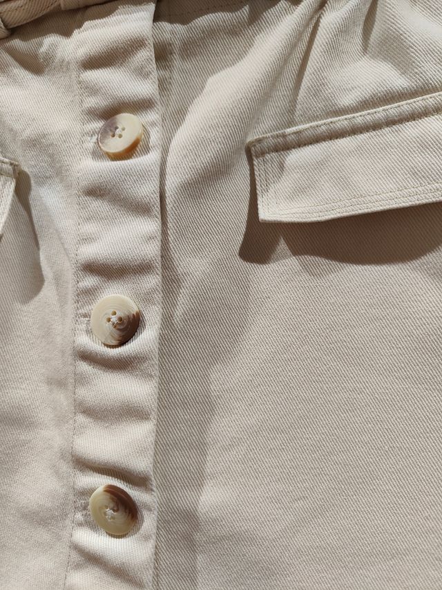 Falda vaquera corta beige con cinturón.