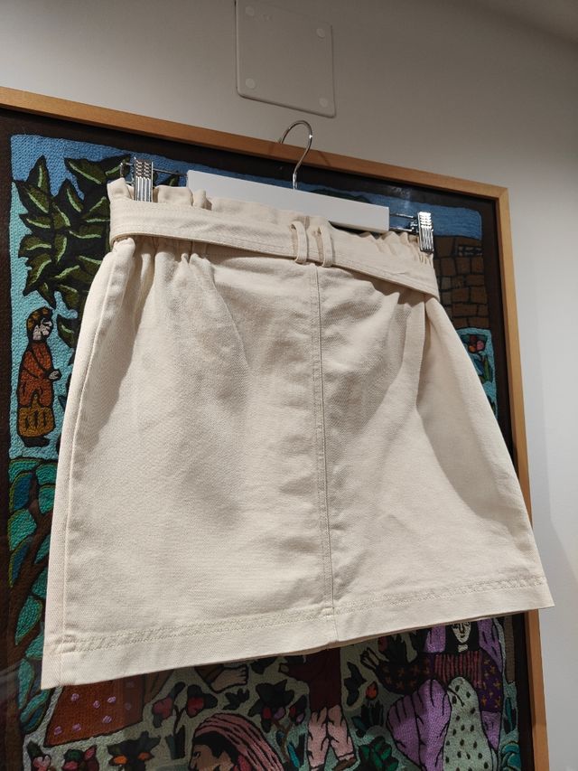Falda vaquera corta beige con cinturón.