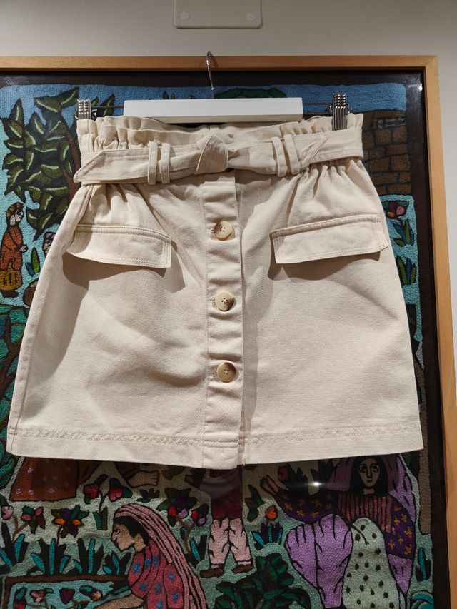 Falda vaquera corta beige con cinturón.