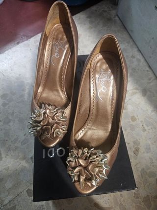 Zapatos de tacón dorados con flor.