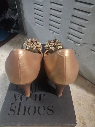 Zapatos de tacón dorados con flor.