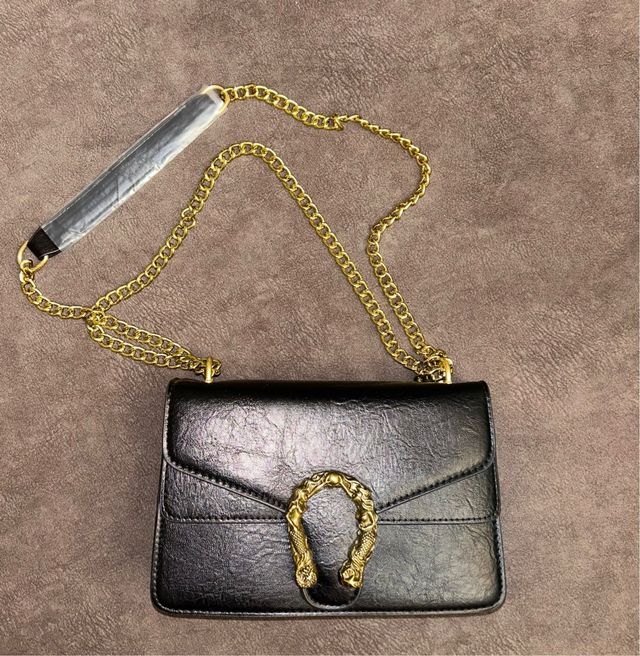 Bolso negro de hombro con asa de cadena dorada.