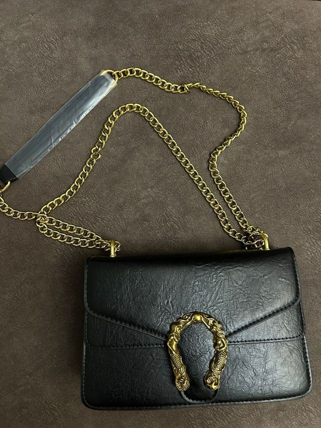 Bolso negro de hombro con asa de cadena dorada.