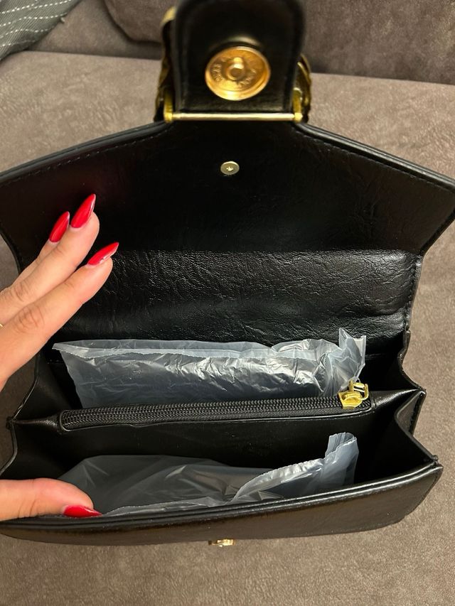 Bolso negro de hombro con asa de cadena dorada.