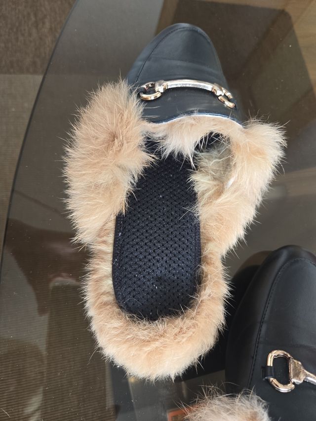 Zapatillas de pelo negras con detalle dorado.