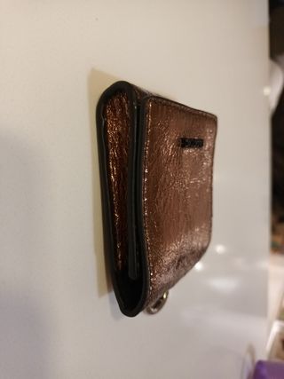 Cartera Parfois dorada con anilla para colgar.
