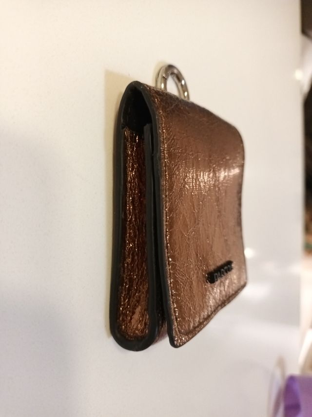 Cartera Parfois dorada con anilla para colgar.