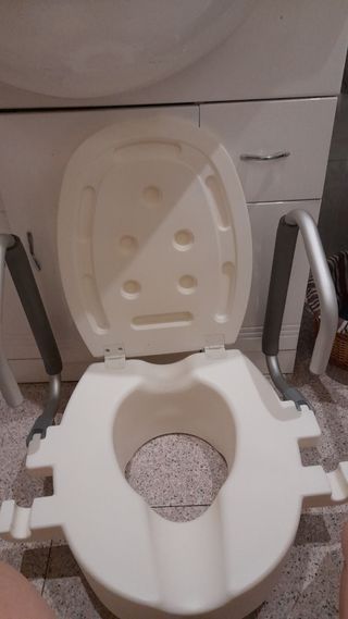 Asiento elevador para inodoro con reposabrazos.