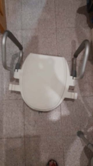 Asiento elevador para inodoro con reposabrazos.