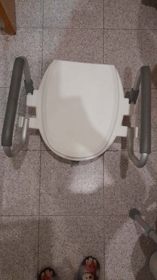 Asiento elevador para inodoro con reposabrazos.