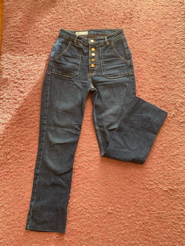 Pantalón vaquero oscuro con botones dorados.