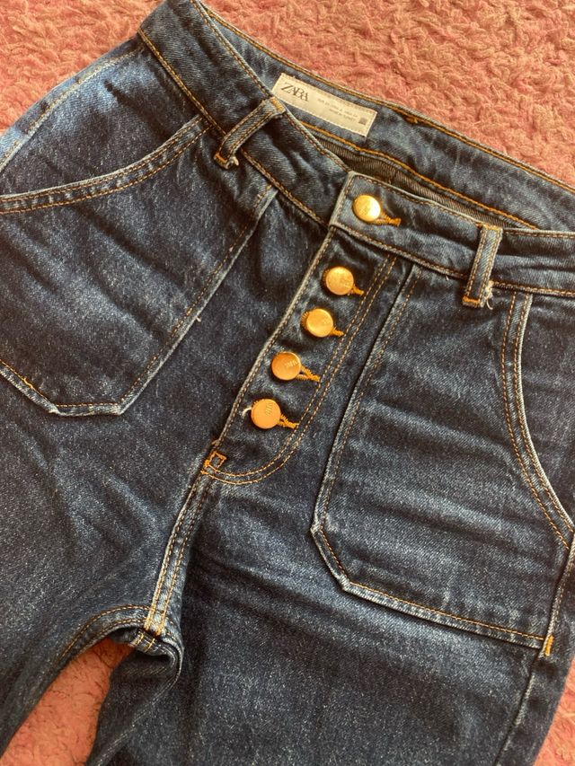 Pantalón vaquero oscuro con botones dorados.