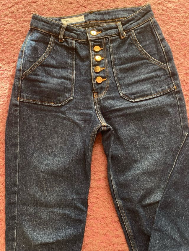 Pantalón vaquero oscuro con botones dorados.