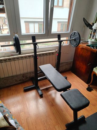 Banco de gimnasio con barra y discos 