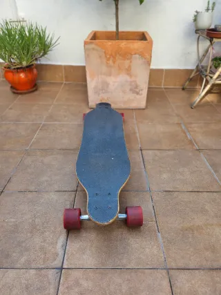 Longboard skate con ruedas de color rojo.