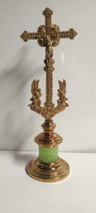 Crucifijo de latón con ángeles y base verde.