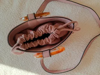 Bolso rosa con anillas y cinta para colgar.