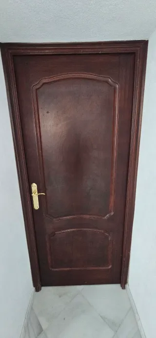 Puerta de madera oscura con manilla dorada.