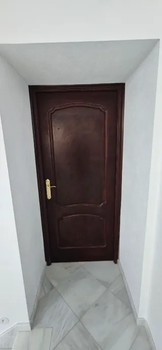Puerta de madera oscura con manilla dorada.