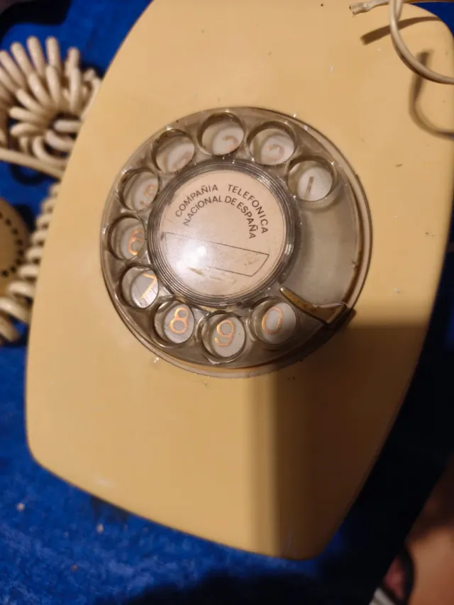 Teléfono antiguo de disco beige de pared.