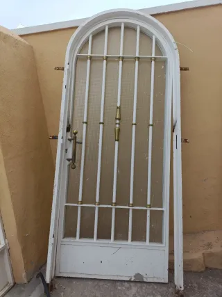 Puerta de entrada con reja y cristal. Con marco.