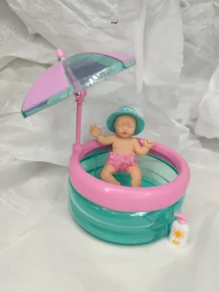 Muñeca bebé con piscina, gorro y crema solar.