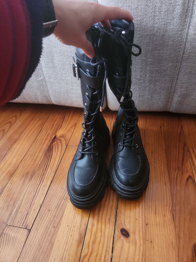 Botas altas negras con cordones y hebilla.