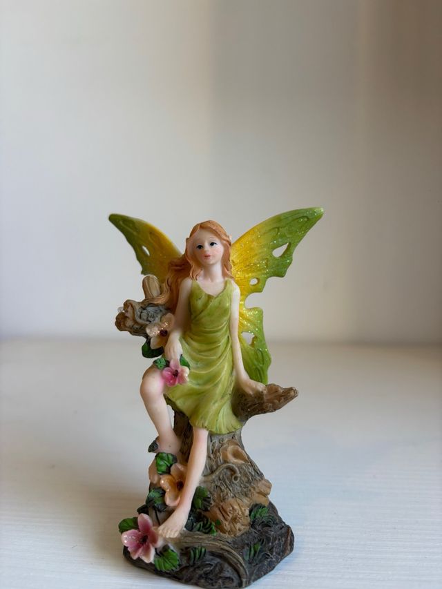 Fatina verde seduta su tronco con fiori