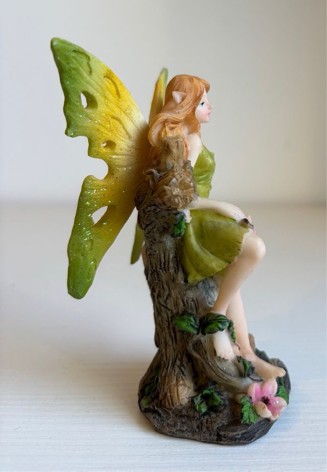 Fatina verde seduta su tronco con fiori