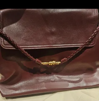 Bolso de mano color burdeos con detalle dorado.
