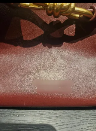 Bolso de mano color burdeos con detalle dorado.
