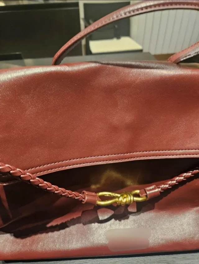 Bolso de mano color burdeos con detalle dorado.