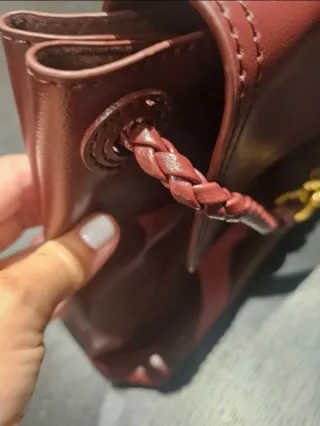 Bolso de mano color burdeos con detalle dorado.
