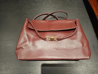 Bolso de mano color burdeos con detalle dorado.
