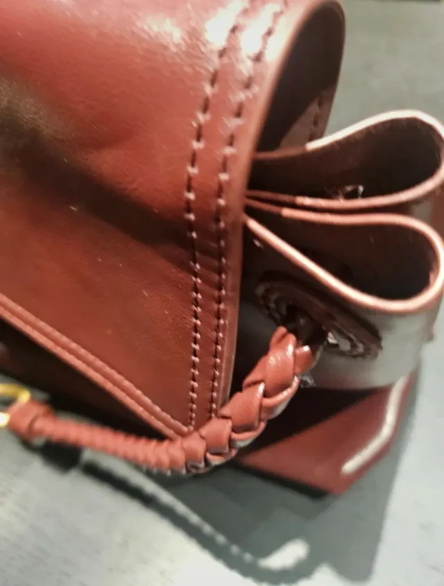 Bolso de mano color burdeos con detalle dorado.