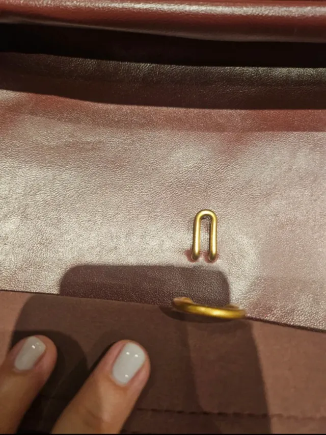 Bolso de mano color burdeos con detalle dorado.