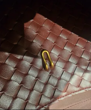 Bolso de mano color burdeos con detalle dorado.
