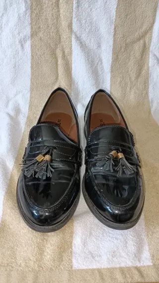 Zapatos charol negros con borlas.