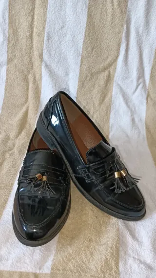 Zapatos charol negros con borlas.